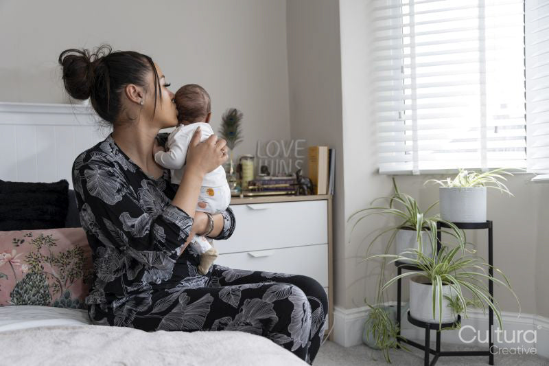 Mother carrying newborn baby girl while sitting on bed at home