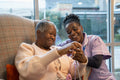 Smiling nurse looking at senior woman knitting in nursing home