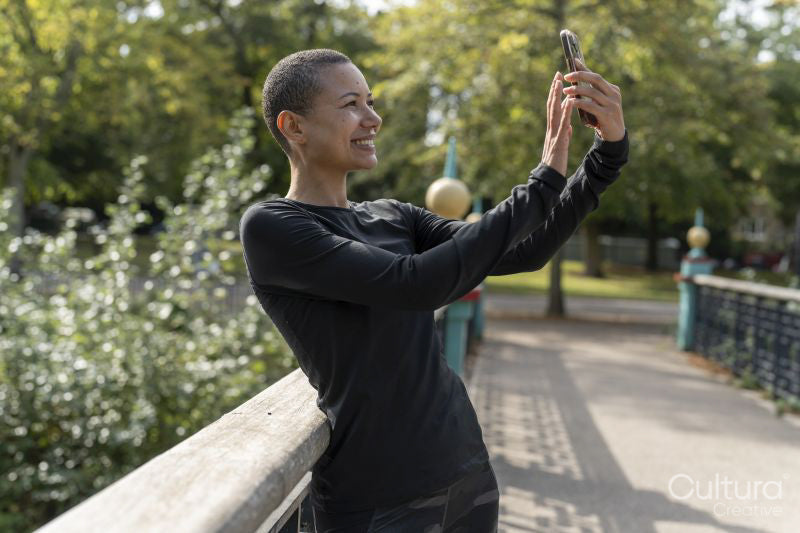 Smiling athletic woman taking selfie with smart phone on footbridge