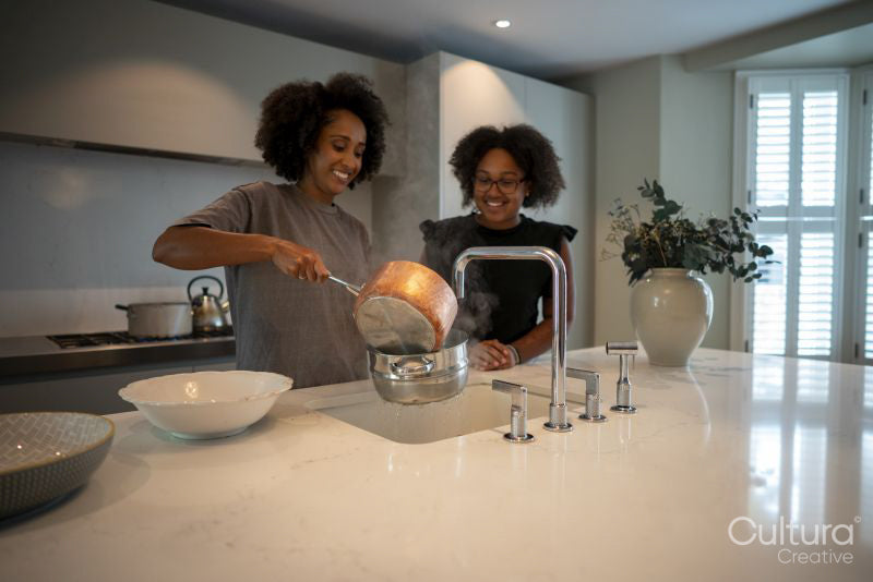 Smiling mother and daughter draining pasta at kitchen sink