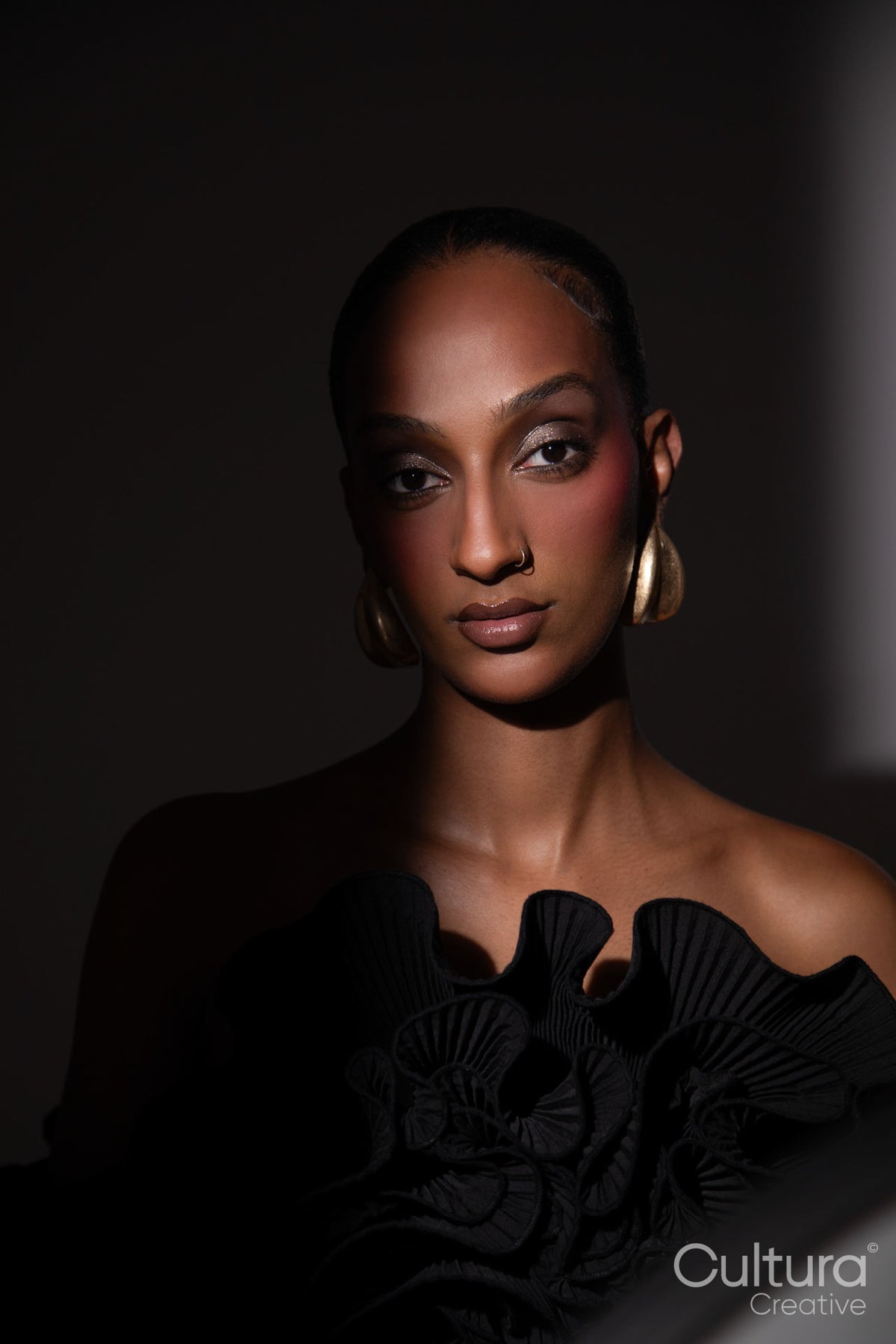 Woman in a black dress with gold earrings on a grey background