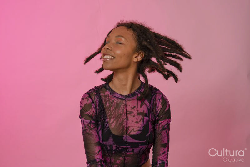 Smiling young woman shaking hair against pink background