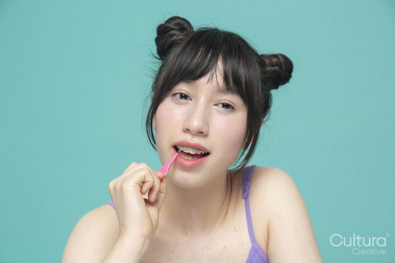 Studio portrait of girl brushing braces with interdental brush