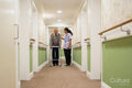 Care giver assisting senior man while walking along corridor in nursing home