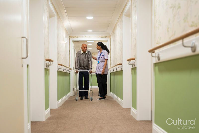 Care giver assisting senior man while walking along corridor in nursing home