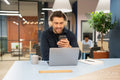 Businessman using phone and laptop in modern office