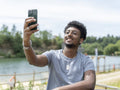 Smiling man taking selfie by lake on sunny day