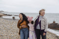 Grandmother, mother and daughter laughing while walking on beach on cloudy day