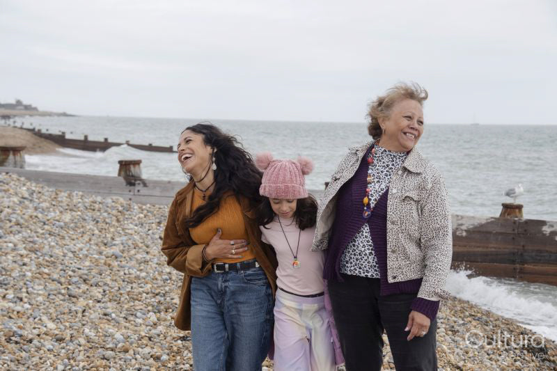 Grandmother, mother and daughter laughing while walking on beach on cloudy day