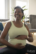 Smiling pregnant woman sitting on yoga mat, touching belly