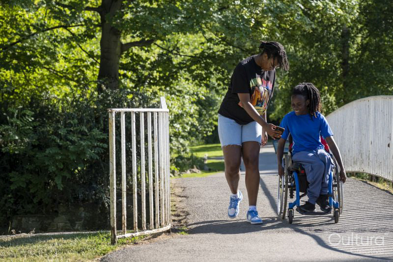 Teenage girl in wheelchair with friend walking in park