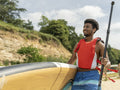 Young man carrying paddleboard and oar on beach