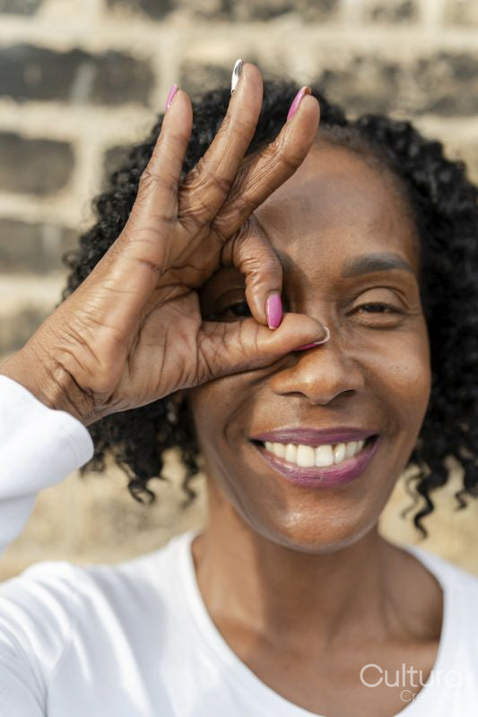 Portrait of woman looking through OK sign made with fingers against brick wall