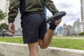 Mid section of man in sports clothing stretching leg in city
