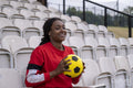 Smiling athletic woman sitting on chair at stadium with soccer ball