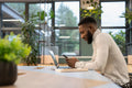 Young man using phone and laptop in office