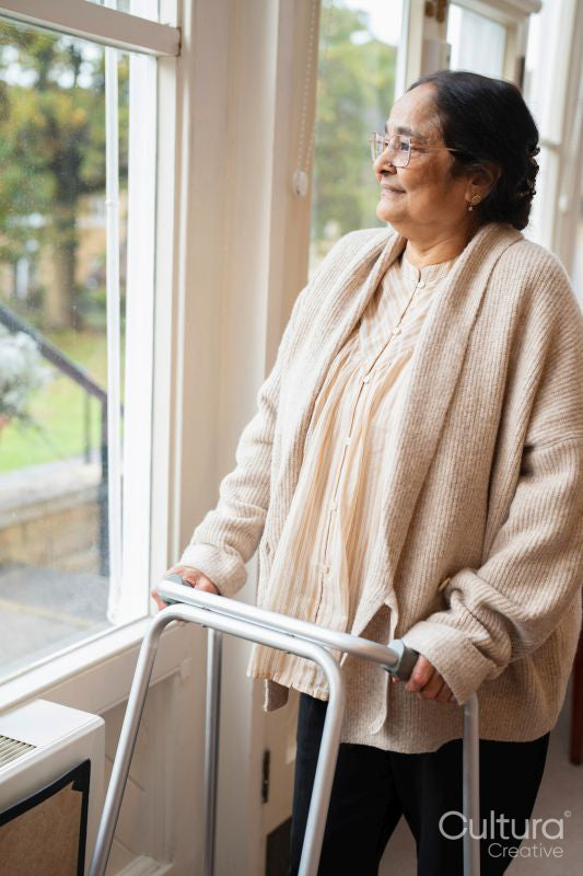 Senior woman using mobility walker and looking through window in nursing home