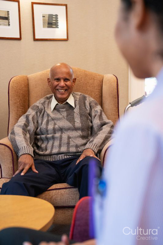 Smiling senior man sitting in armchair and looking at nurse