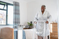 Smiling senior woman in bathrobe walking with mobility walker in bedroom