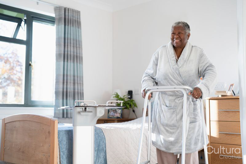 Smiling senior woman in bathrobe walking with mobility walker in bedroom