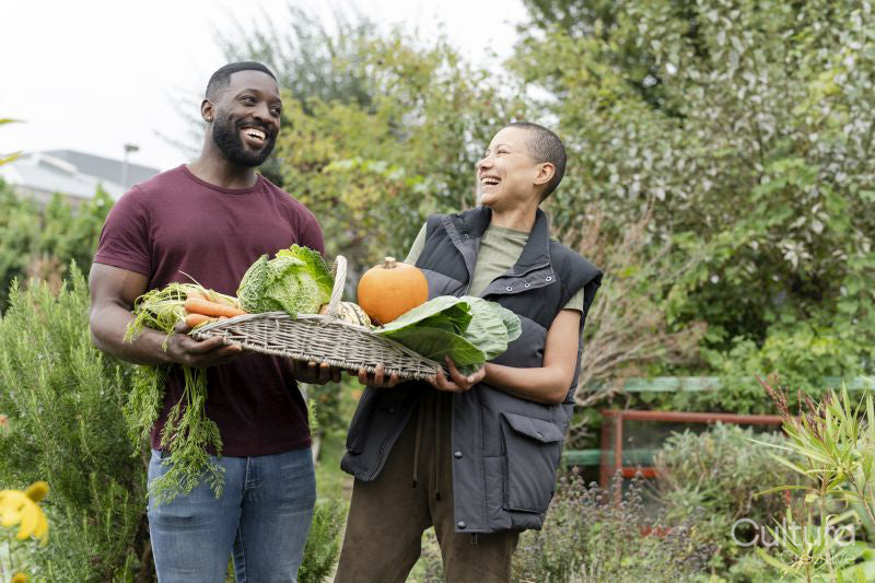 Portrait of smiling couple holding basket with fresh vegetables in urban garden