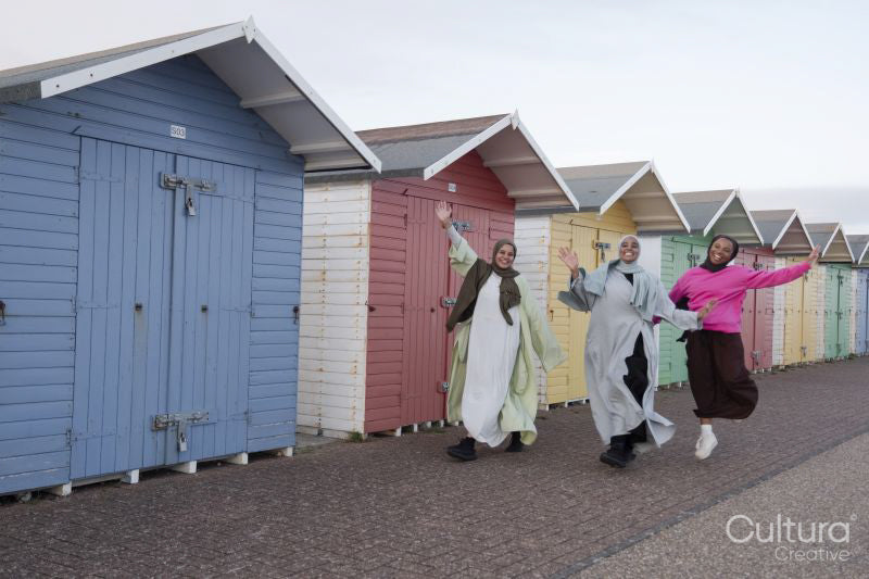 Cheerful Muslim friends waving while walking next to beach huts