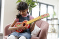Little girl playing on ukulele in living room