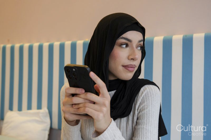 Young woman in hijab using phone in cafe