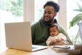 Father holding baby daughter and using laptop at home