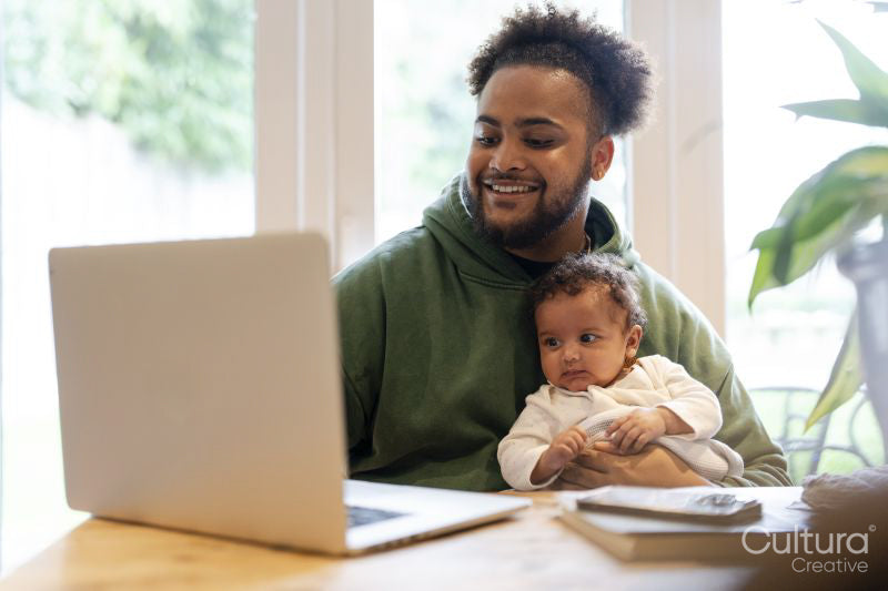 Father holding baby daughter and using laptop at home