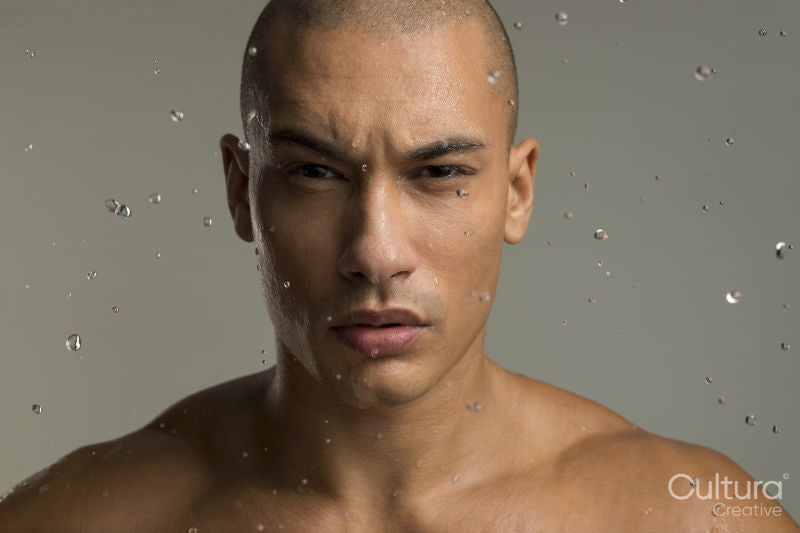Studio portrait of shirtless man splashing water on face