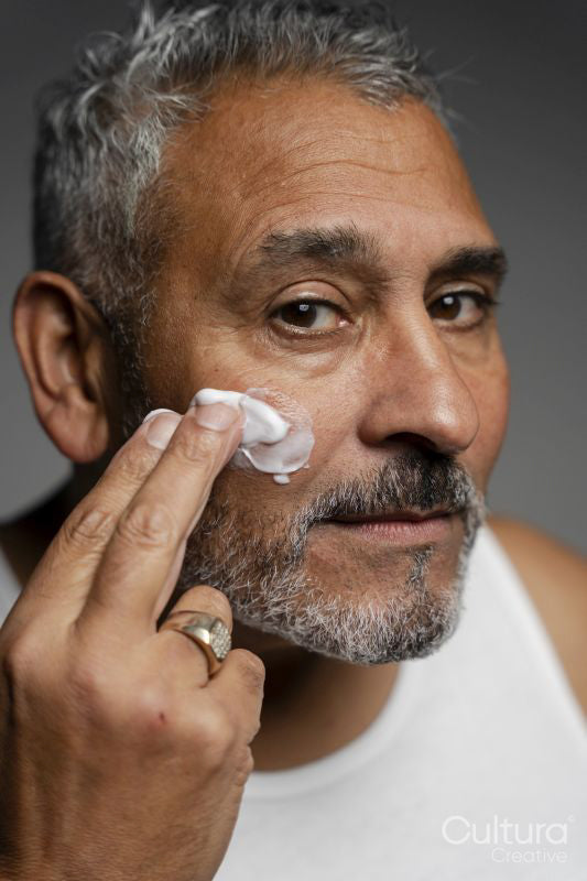 Portrait of man applying face cream against gray background