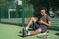 Smiling man sitting in tennis court, looking at smart phone