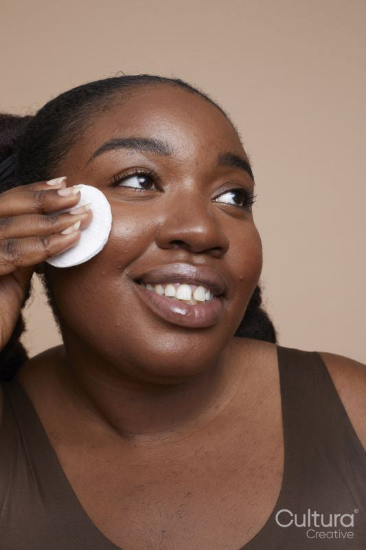 Studio shot of smiling young woman removing make-up with cotton pad