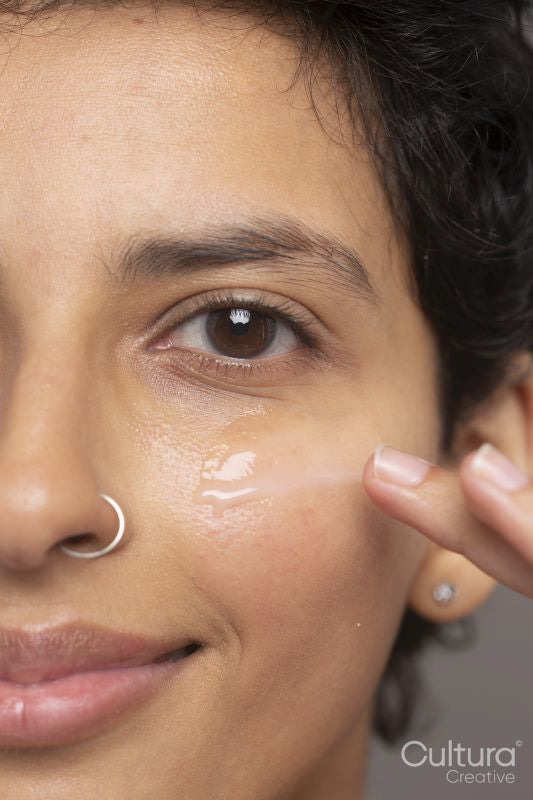 Close-up of smiling woman applying moisturizer on face