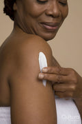 Studio shot of mature woman applying body lotion on shoulder