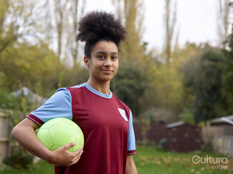 Portrait of female soccer player with ball outdoors