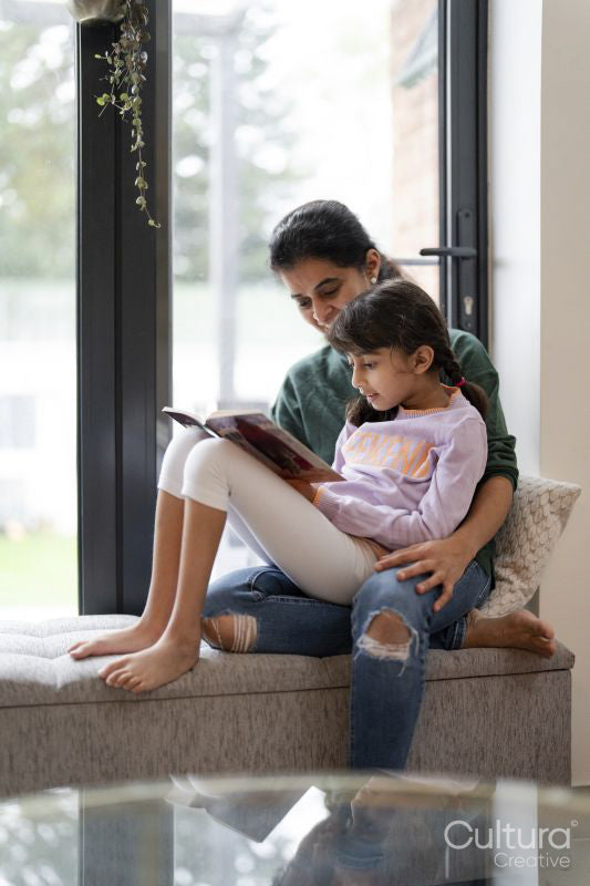 Mother and daughter sitting near window and reading book