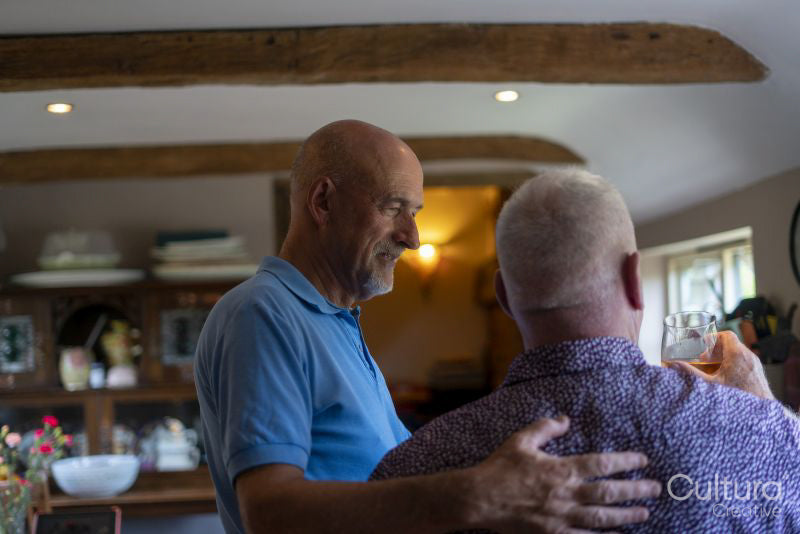 Senior male couple with drinks in kitchen