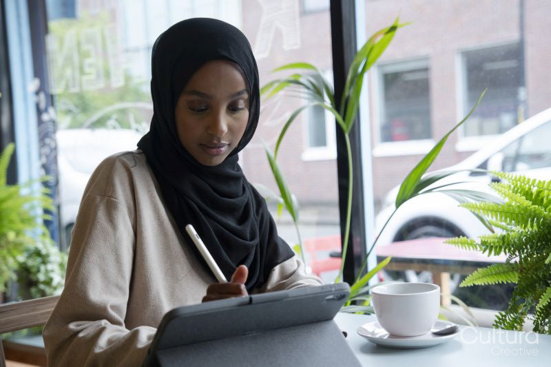 Young woman in hijab working on tablet in cafe