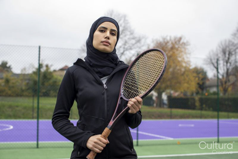 Portrait of woman in black sports clothing and hijab holding tennis racket