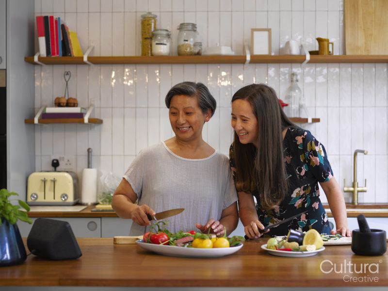 Mother and adult daughter using digital device while preparing food in kitchen