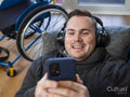 Smiling man with headphones looking at smart phone, wheelchair in background