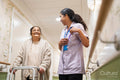 Nurse helping senior lady to walk with mobility walker at nursing home