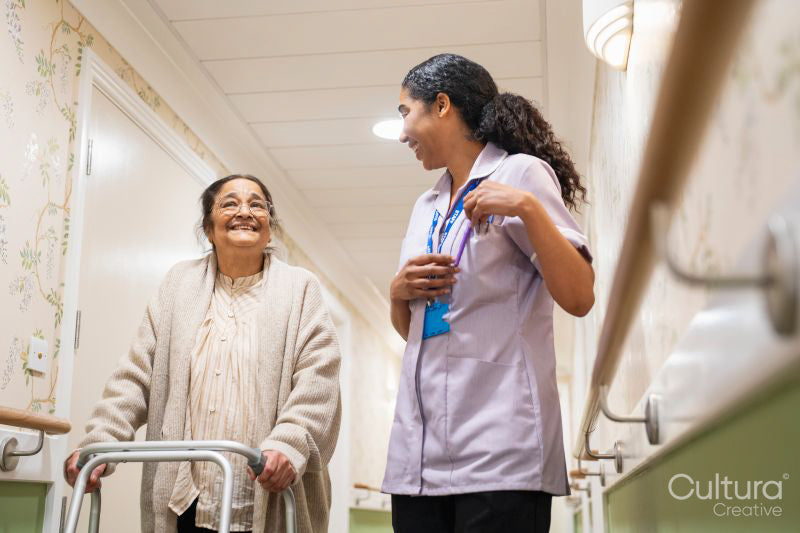 Nurse helping senior lady to walk with mobility walker at nursing home
