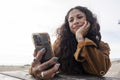 Smiling woman using smart phone while sitting by picnic table on beach