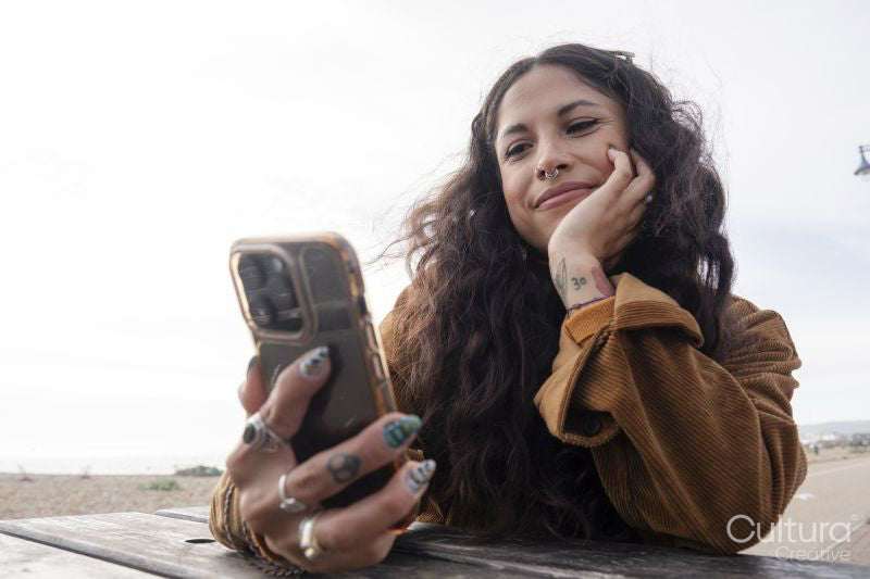 Smiling woman using smart phone while sitting by picnic table on beach