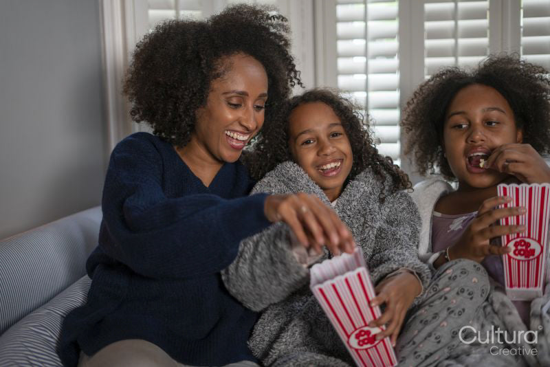 Smiling woman with daughters enjoying popcorn on sofa