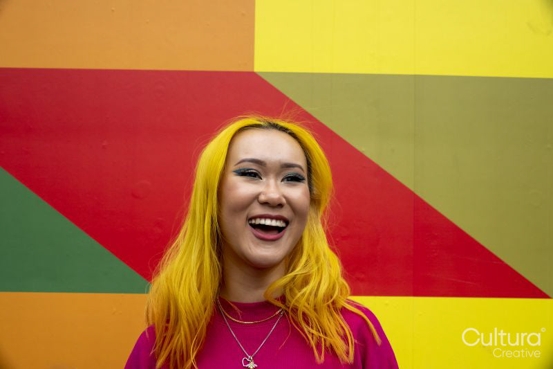 Smiling young woman with yellow hair against colorful wall