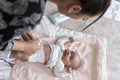 Mother changing diaper to newborn baby girl on bed at home
